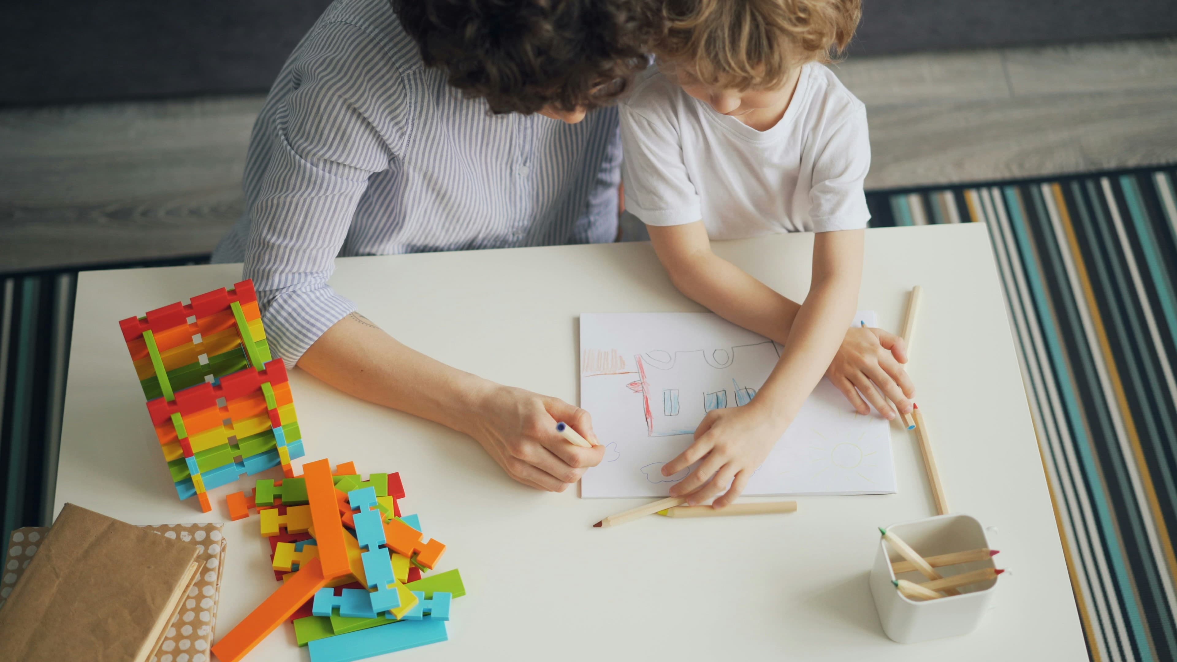 A parent helping a child draw at a table